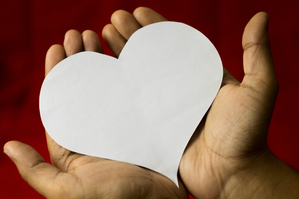 Close-up of hands cradling a heart-shaped paper, symbolizing love on a red background.