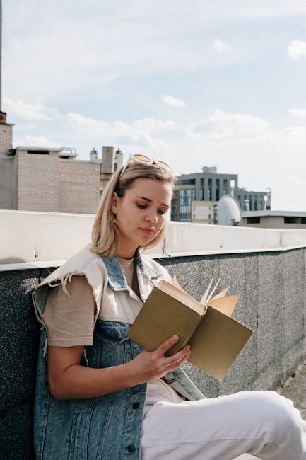 Young blonde woman enjoys reading a book on a sunny rooftop terrace, embracing leisure and literature.